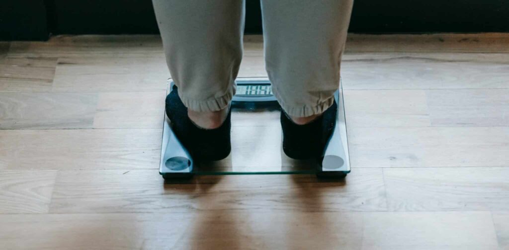 cropped image showing a person experiencing weight gain during peri and menopause, standing on scales wearing track pants and socks.